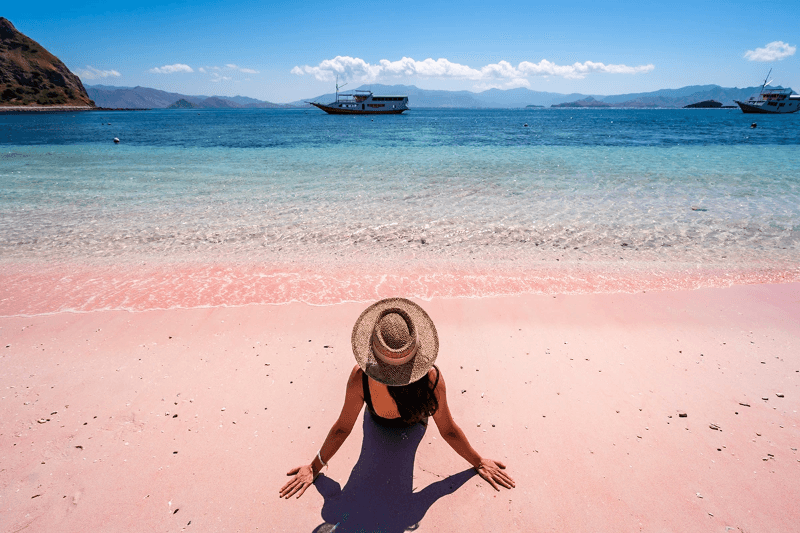 Young female tourism enjoying the tropical pink sandy beach with clear turquoise water at Komodo islands in Indonesia. By kitzstocker